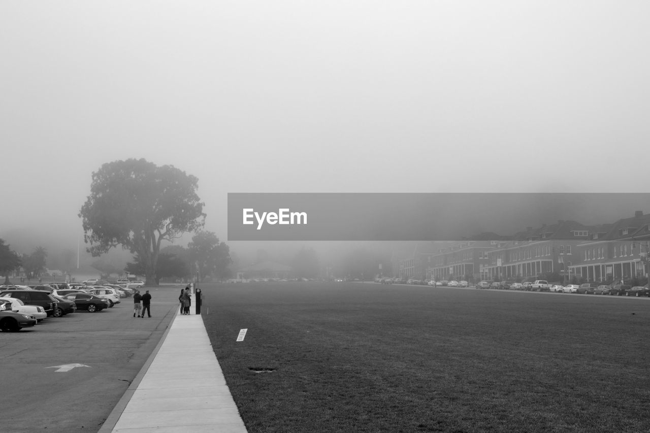 People standing on wall by field in foggy weather