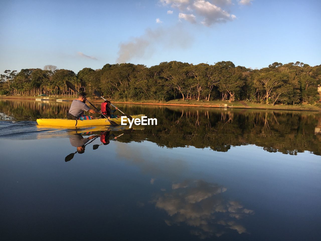 Father and son kayaking on lake against sky