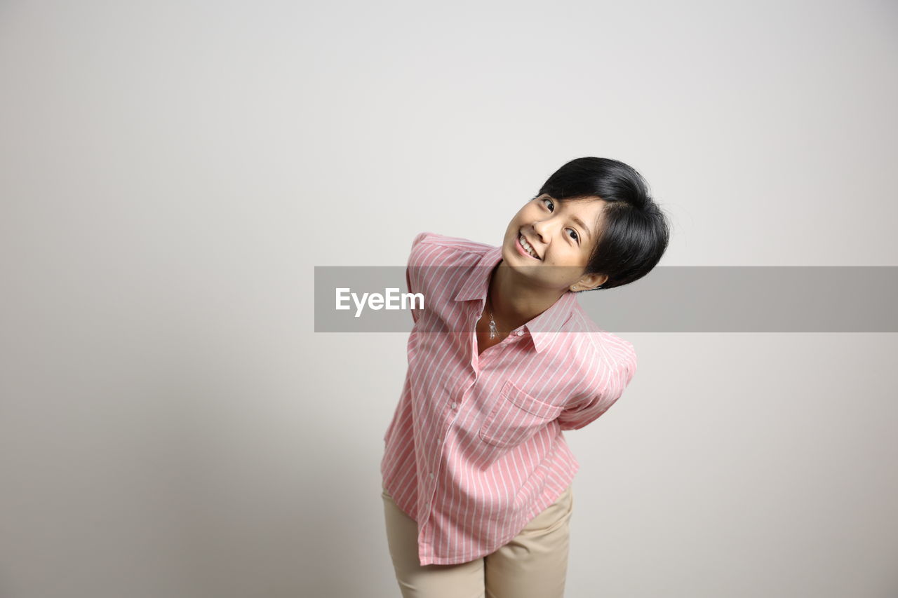 PORTRAIT OF SMILING WOMAN AGAINST WHITE BACKGROUND