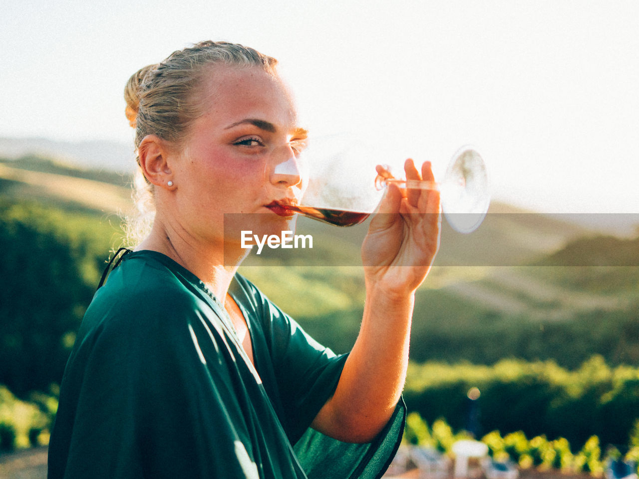 Portrait of woman drinking wine against landscape