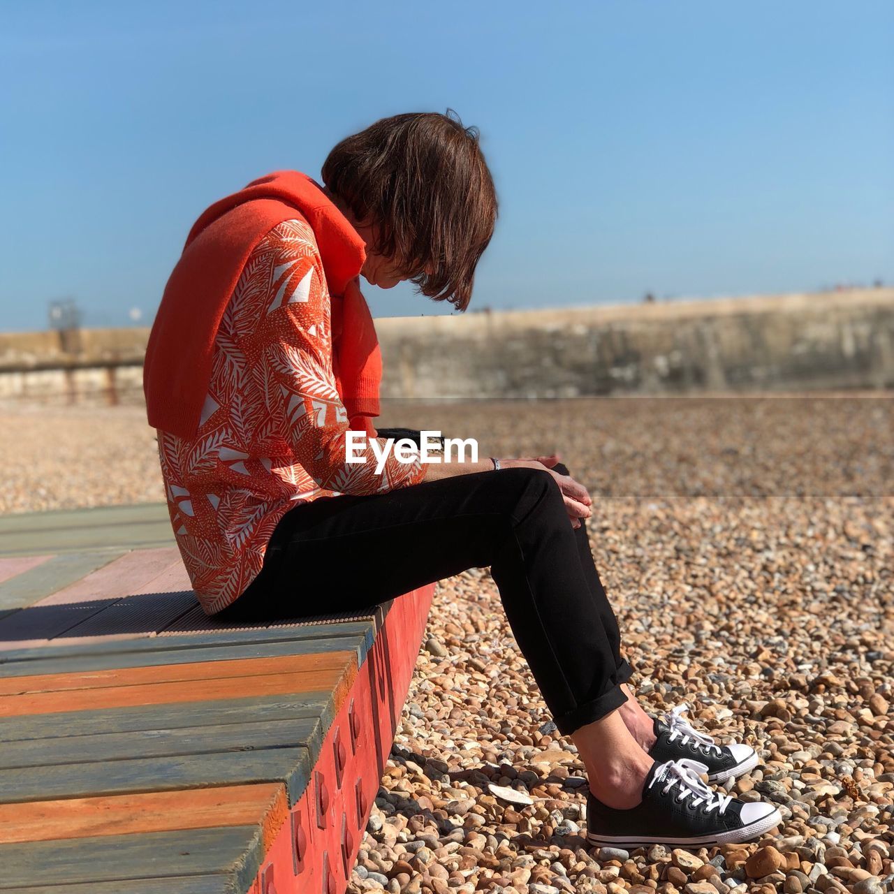 FULL LENGTH OF YOUNG WOMAN SITTING AGAINST SKY