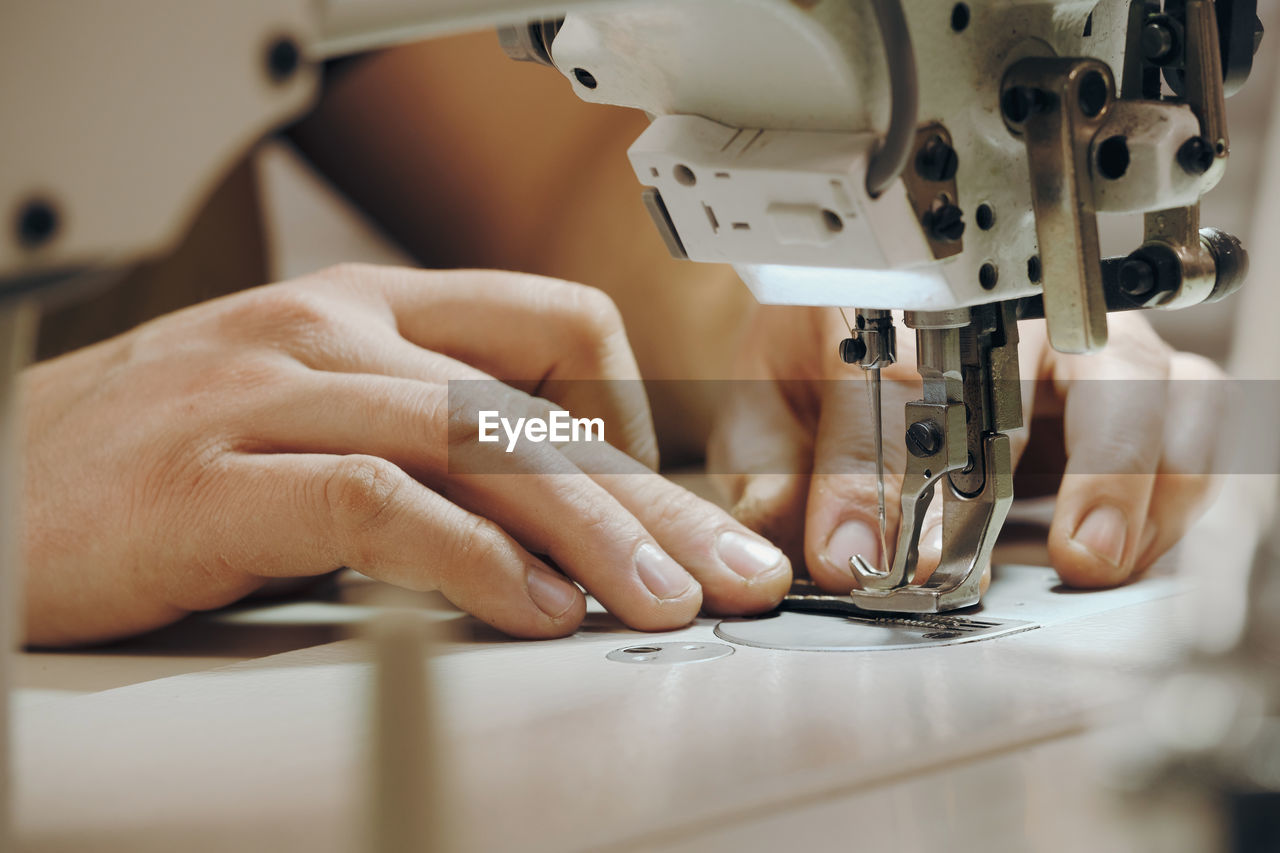 Tailor sewing at workplace. man hands sewing on machine at his studio. tailoring concept. close-up