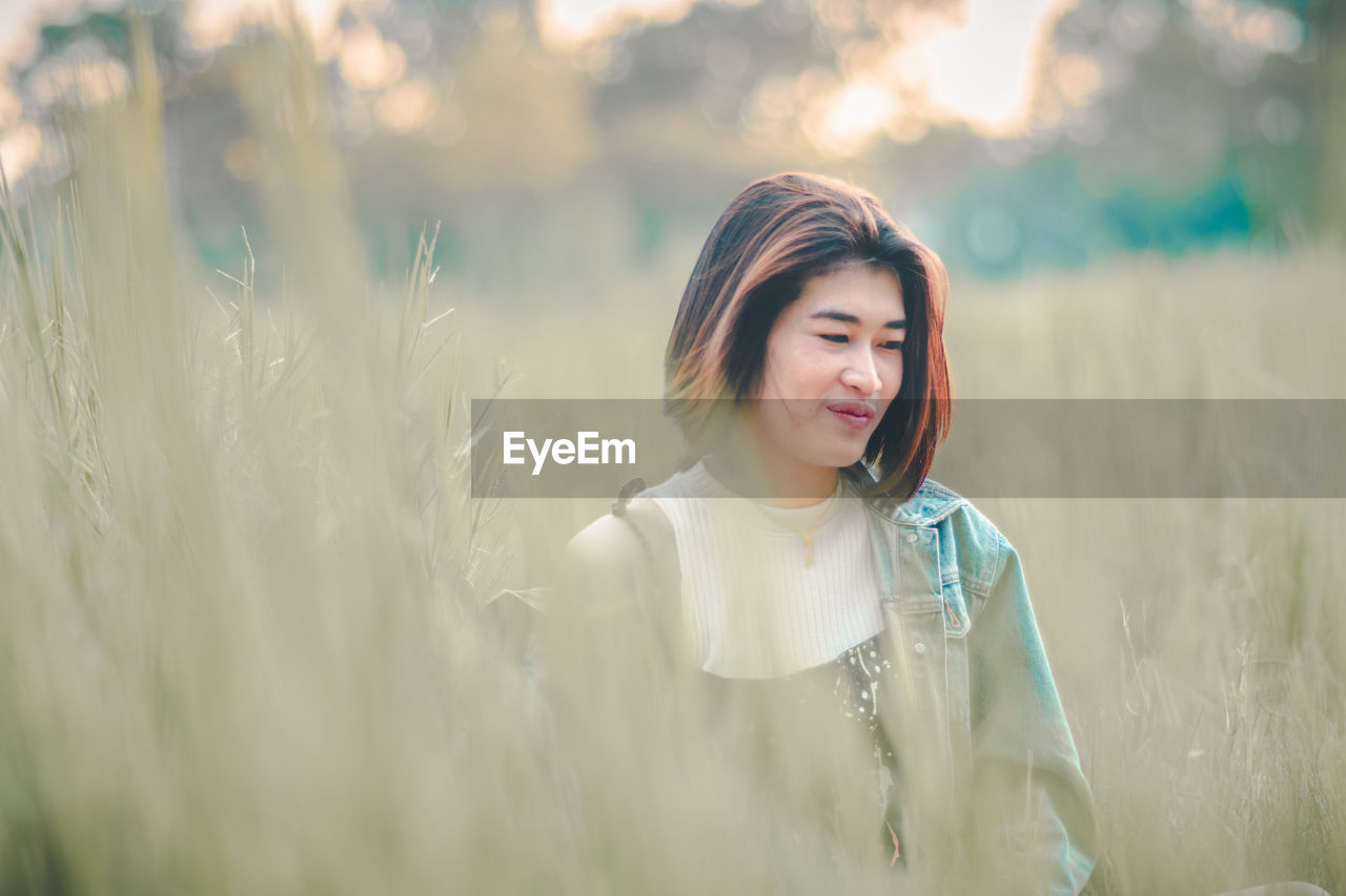 Smiling thoughtful young woman looking away while standing on grassy field