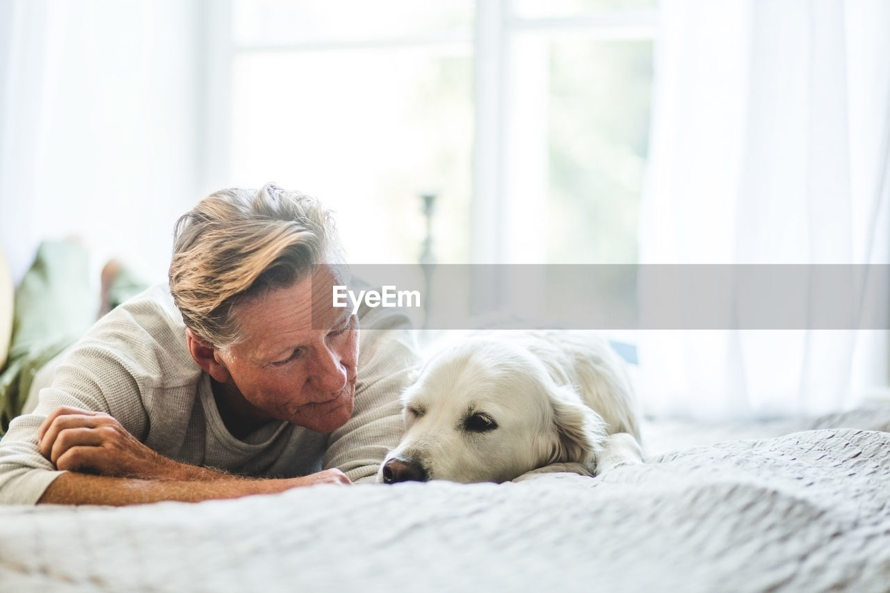 Close-up of senior man looking at cute dog while lying on bed in bedroom