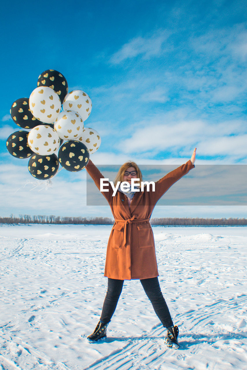 Woman with balloons standing on snow against sky