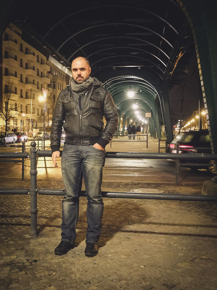 Portrait of man standing by railing on street at night