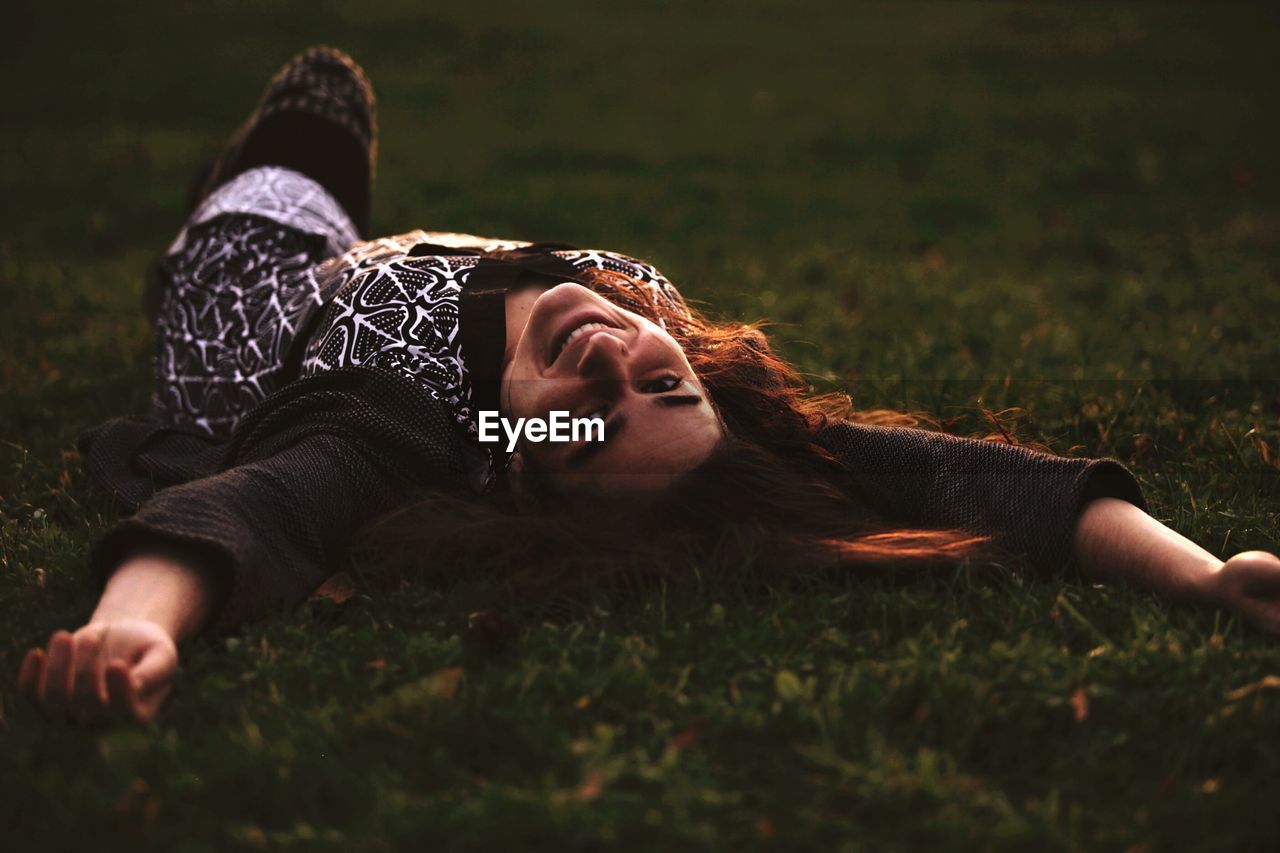 Portrait of beautiful woman lying on grass at park during sunset