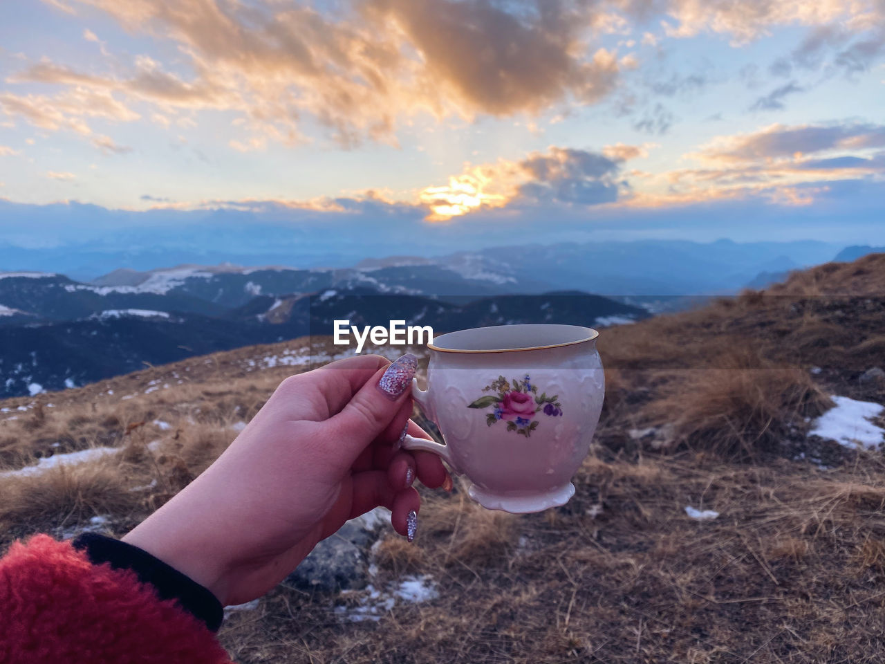 MIDSECTION OF MAN HOLDING ICE CREAM AGAINST MOUNTAINS DURING SUNSET