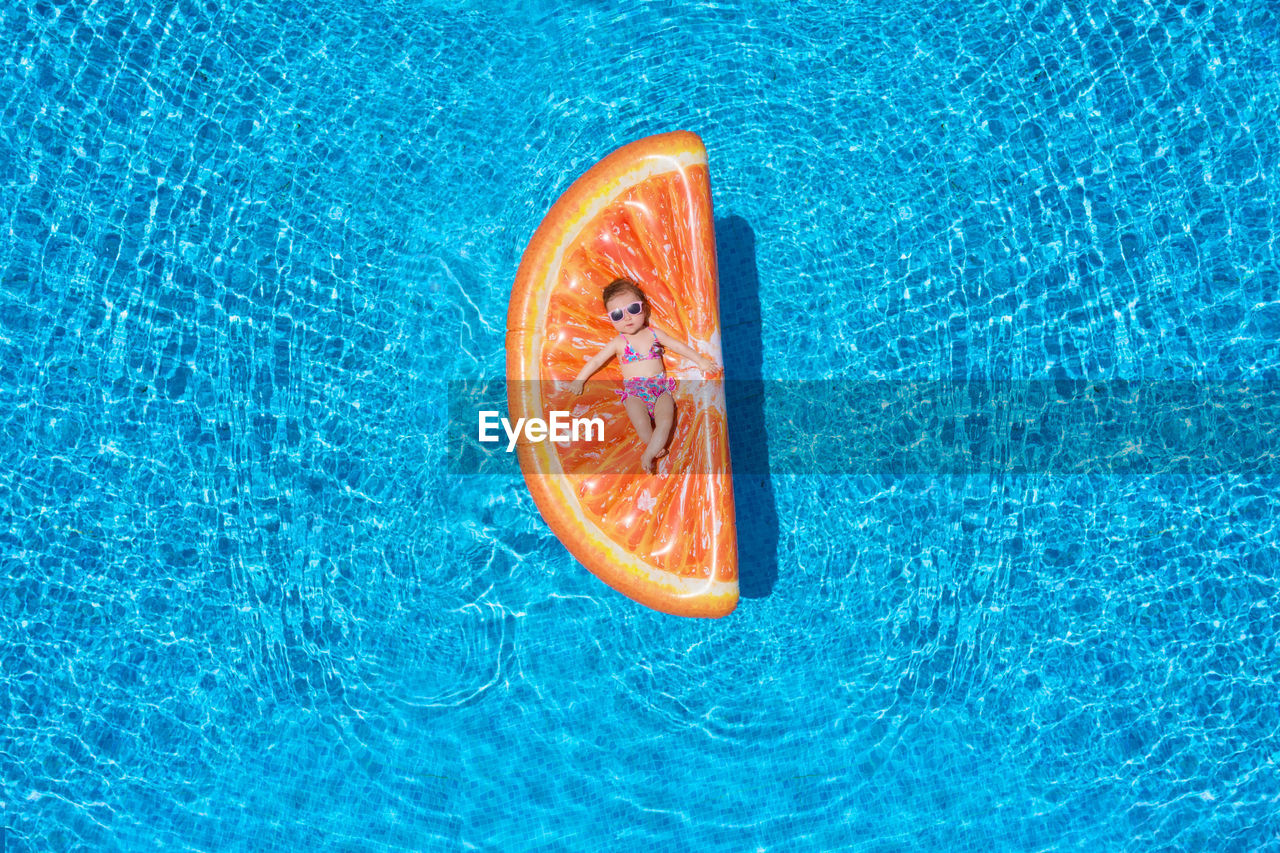 High angle view of baby girl relaxing on orange shaped pool raft