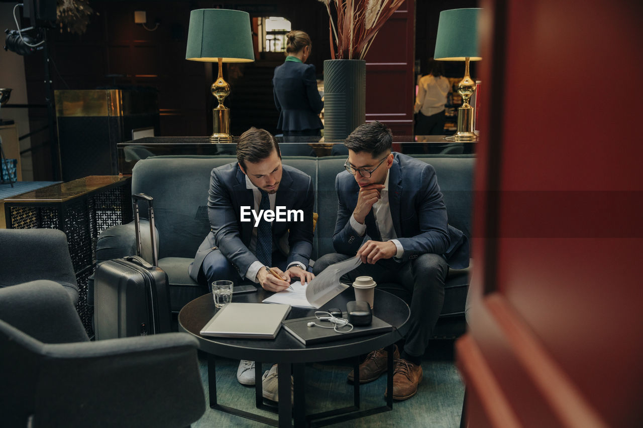 Young businesswoman signing contract while sitting my male colleague in hotel lounge