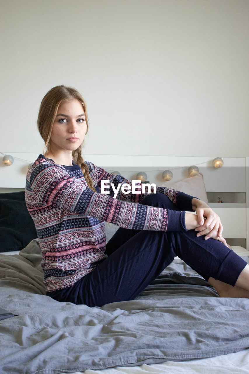 PORTRAIT OF YOUNG WOMAN SITTING ON BED