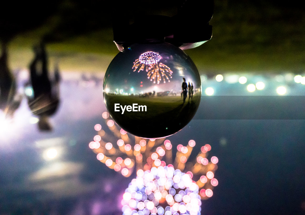 Reflection of firework display on crystal ball on field at night