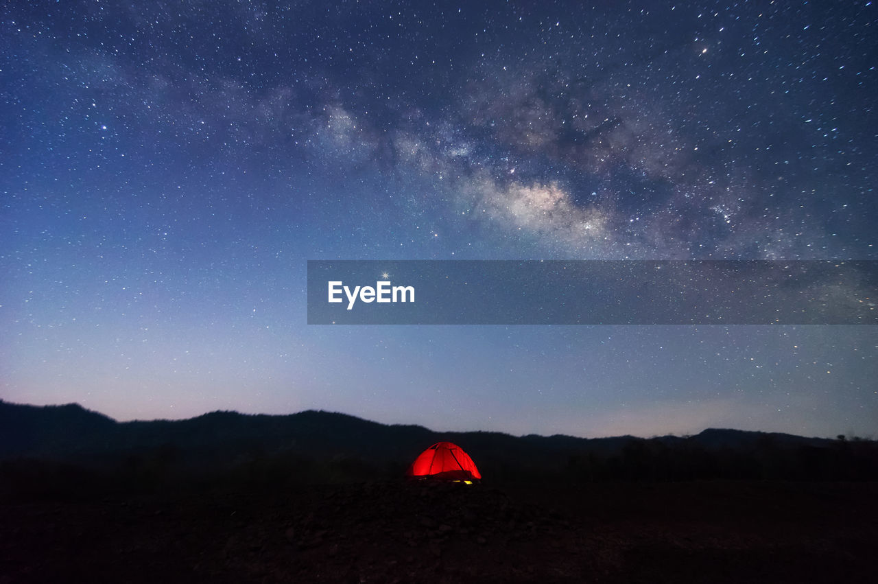 Red tent in reservoir under milky way galaxy with stars space dust in the universe, long exposure. 