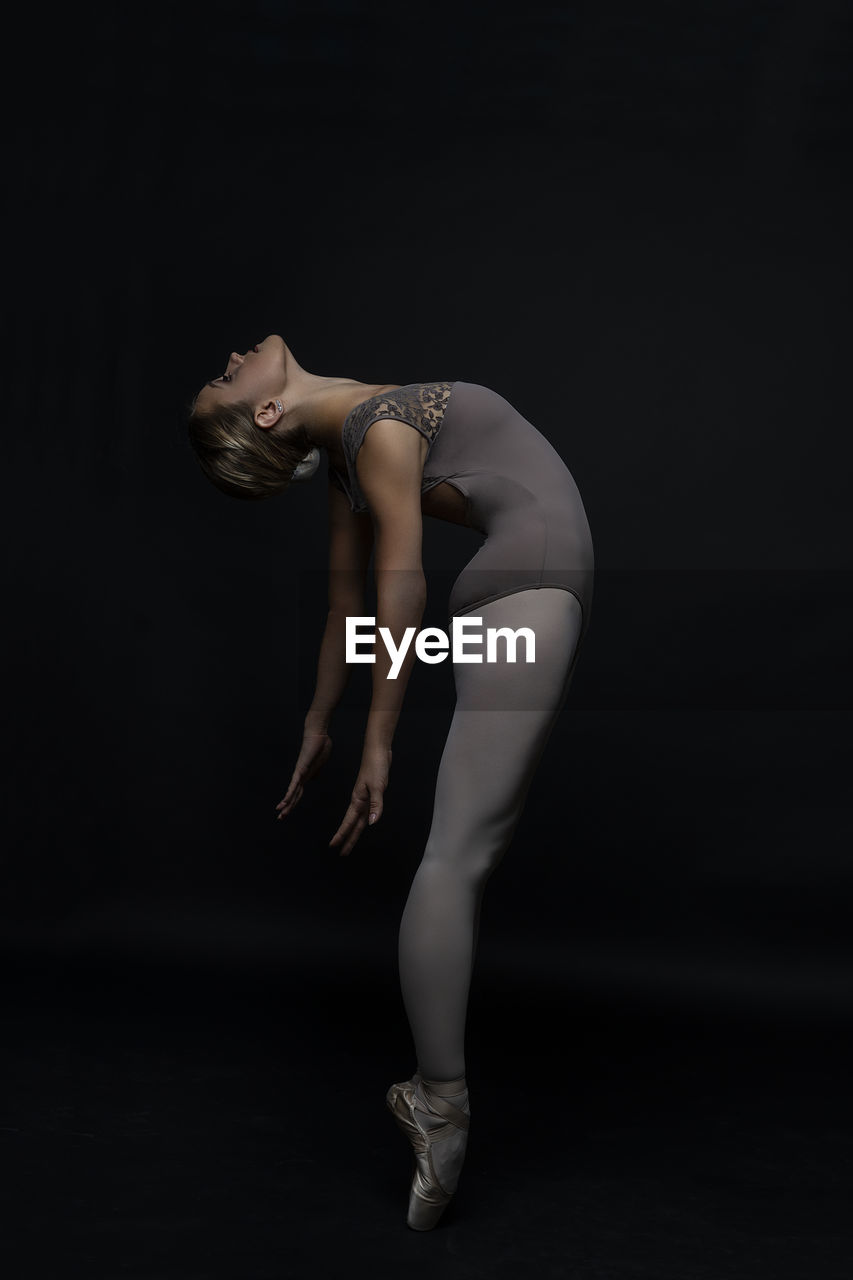 Side view of ballet dancer stretching against black background