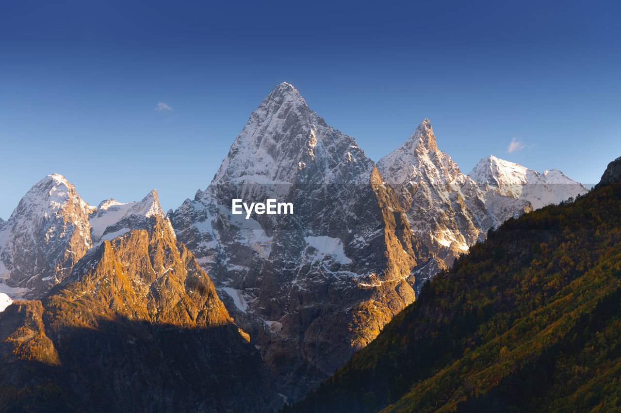 Sharp mountain peaks partially covered with snow and surrounded by rays of sun under a picturesque