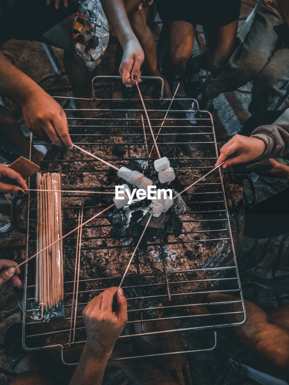 Circle of friends enjoying marshmallows smores over a griller.