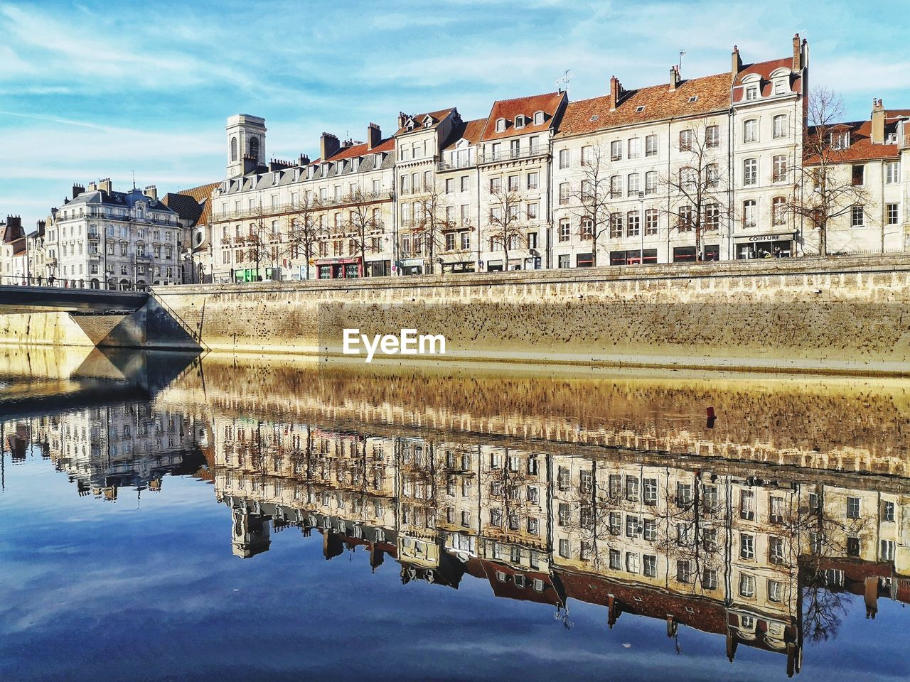 Reflection of buildings on river against sky in city