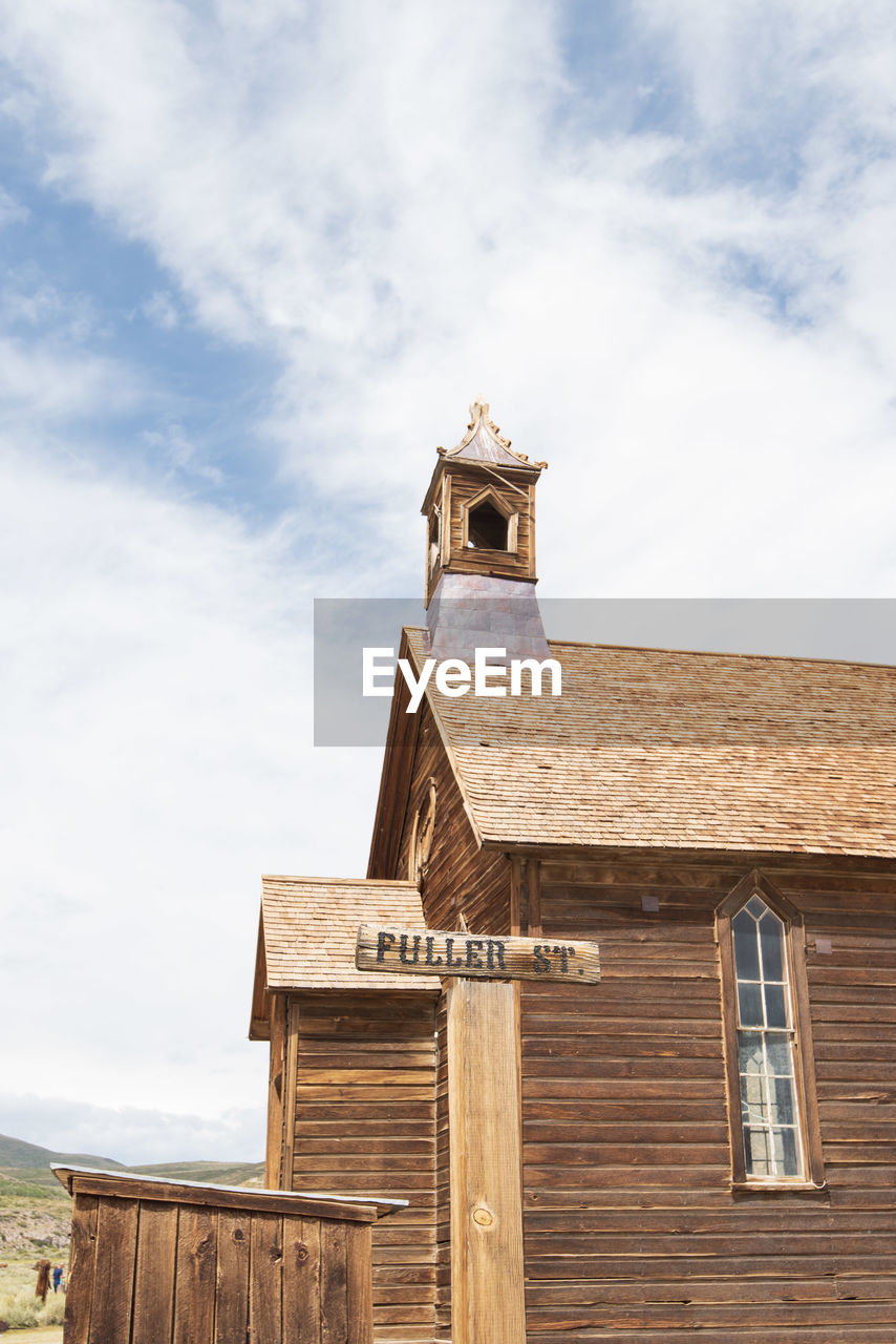 Low angle view of old church building against sky with wooden street sign in ghost town