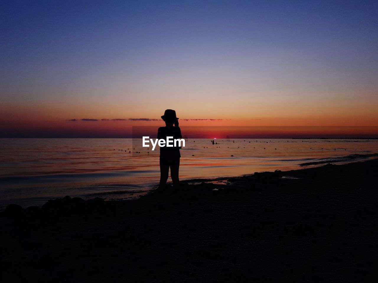 Silhouette boy standing at beach against sky during sunset