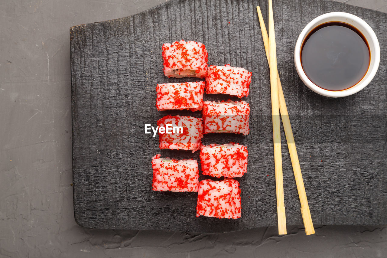 Roll with shrimp cucumber and tobiko caviar and sticks on a black carved board and soy sauce i