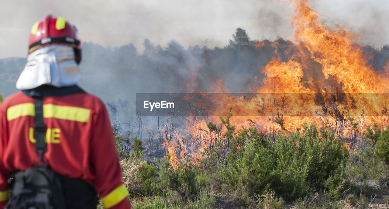 Rear view of firefighter standing against fire on field