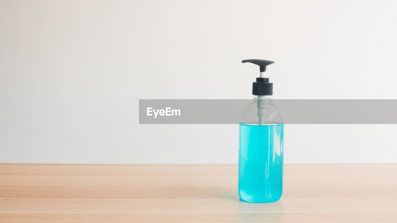 CLOSE-UP OF EMPTY BOTTLE ON TABLE AGAINST WHITE WALL