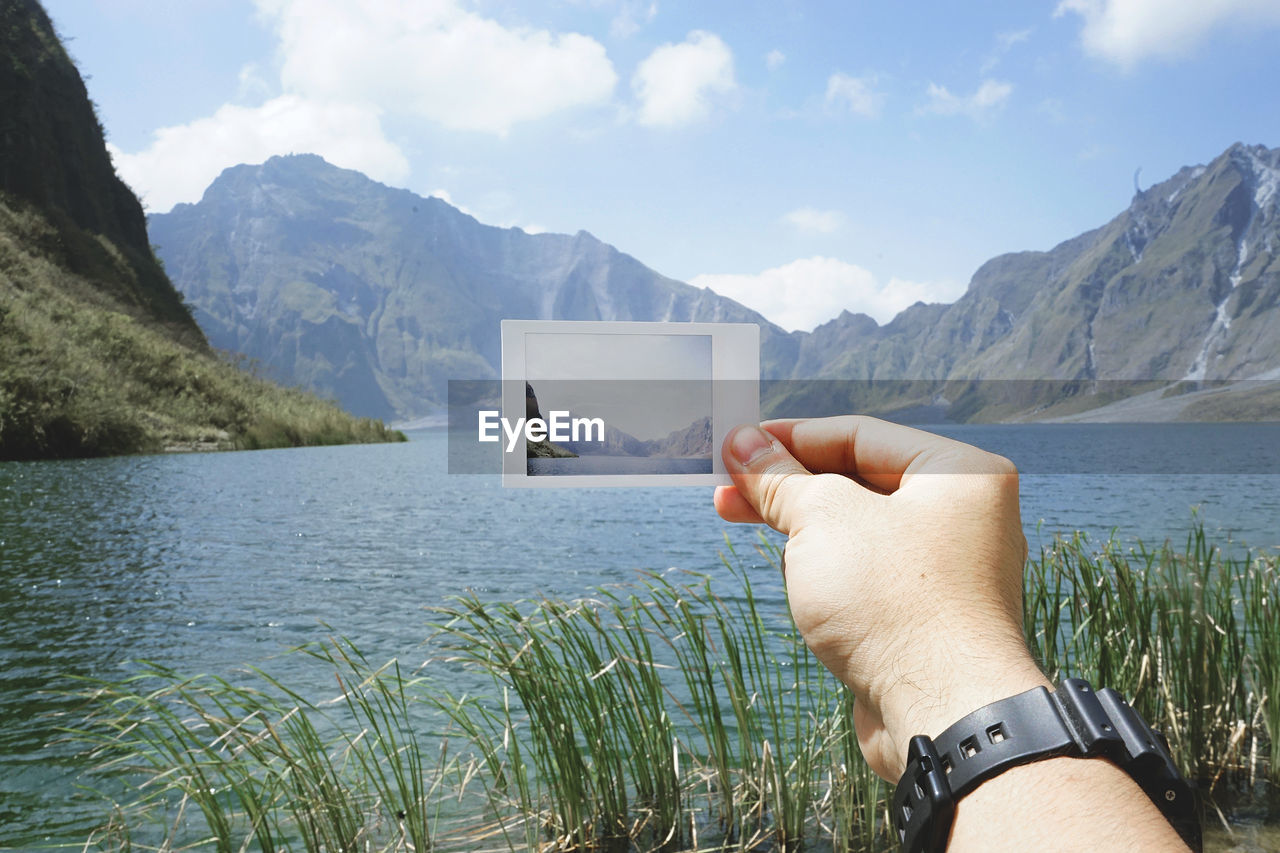 Scenic view of hand holding photograph in front of lake