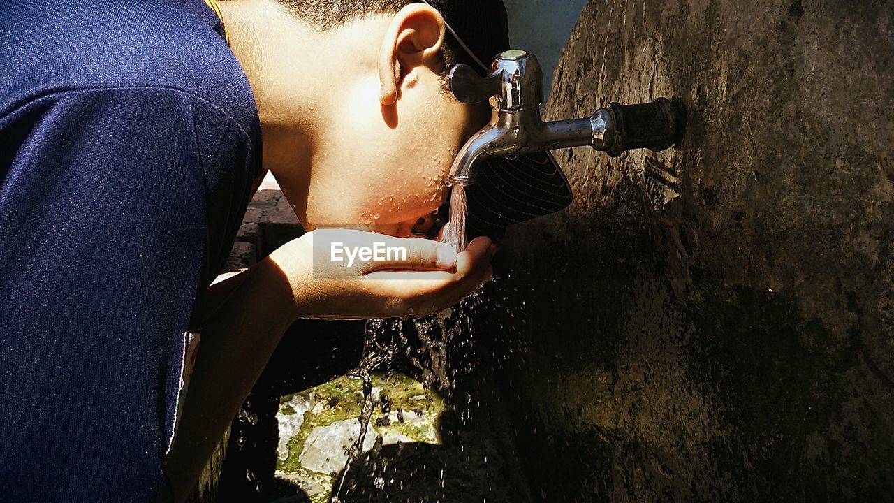 Side view of boy drinking water from faucet