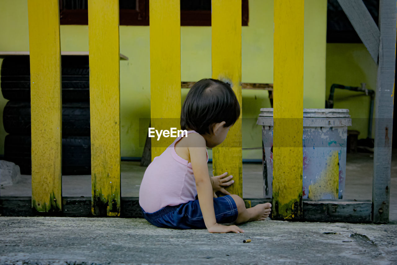 SIDE VIEW OF BOY SITTING ON YELLOW SEAT