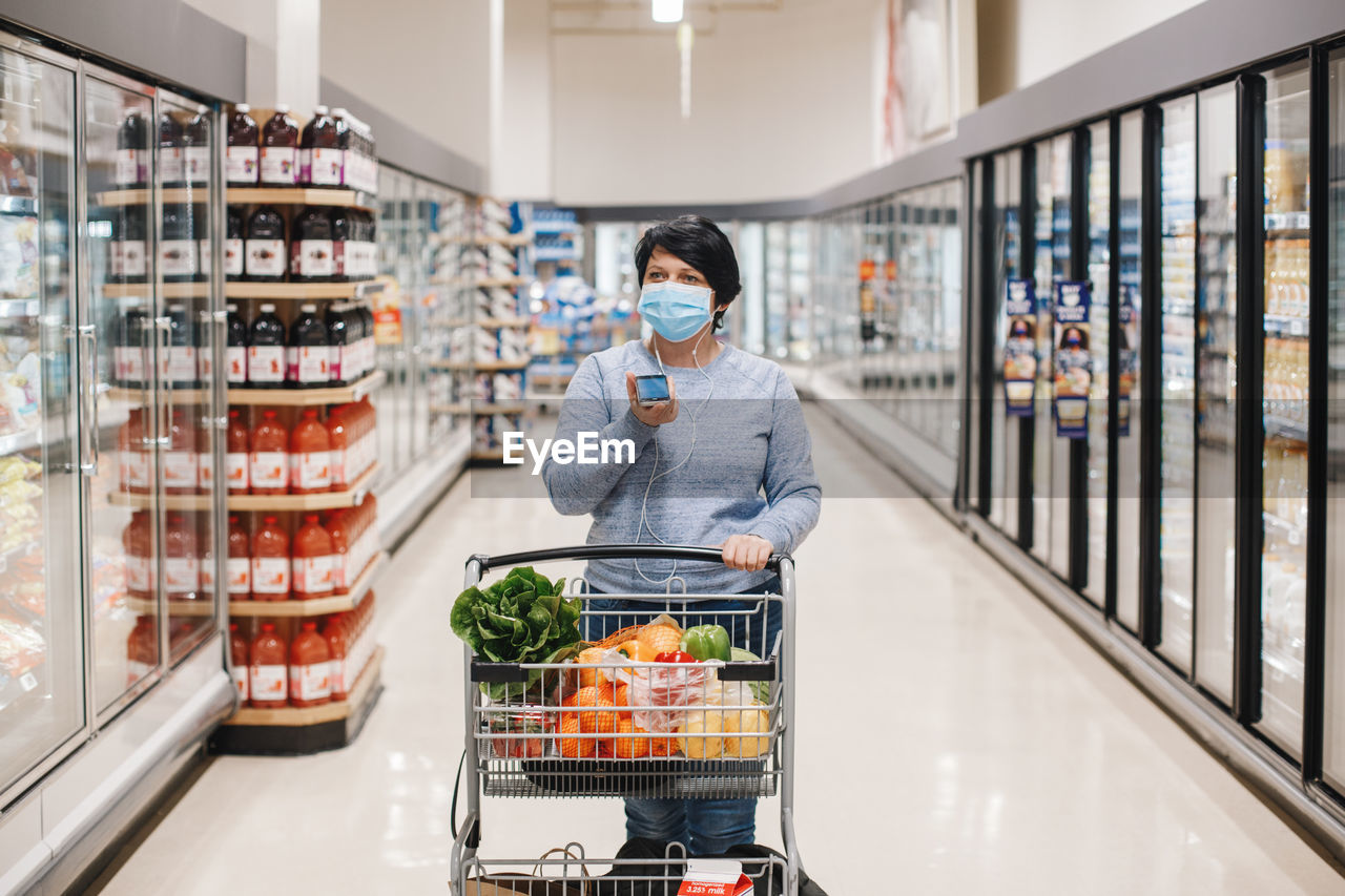 Middle age brunette woman shopping in grocery store supermarket and talking on audio chat phone. 