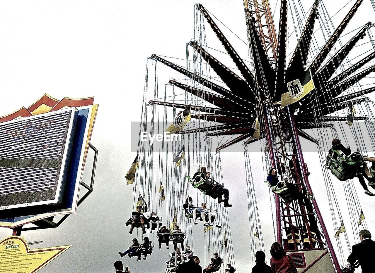 Low angle view of people enjoying chain swing ride against cloudy sky