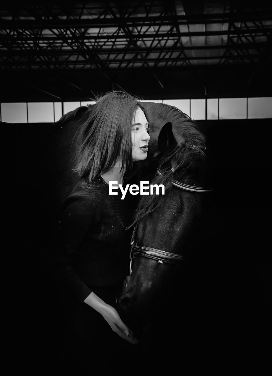 Side view of woman standing with horse in darkroom