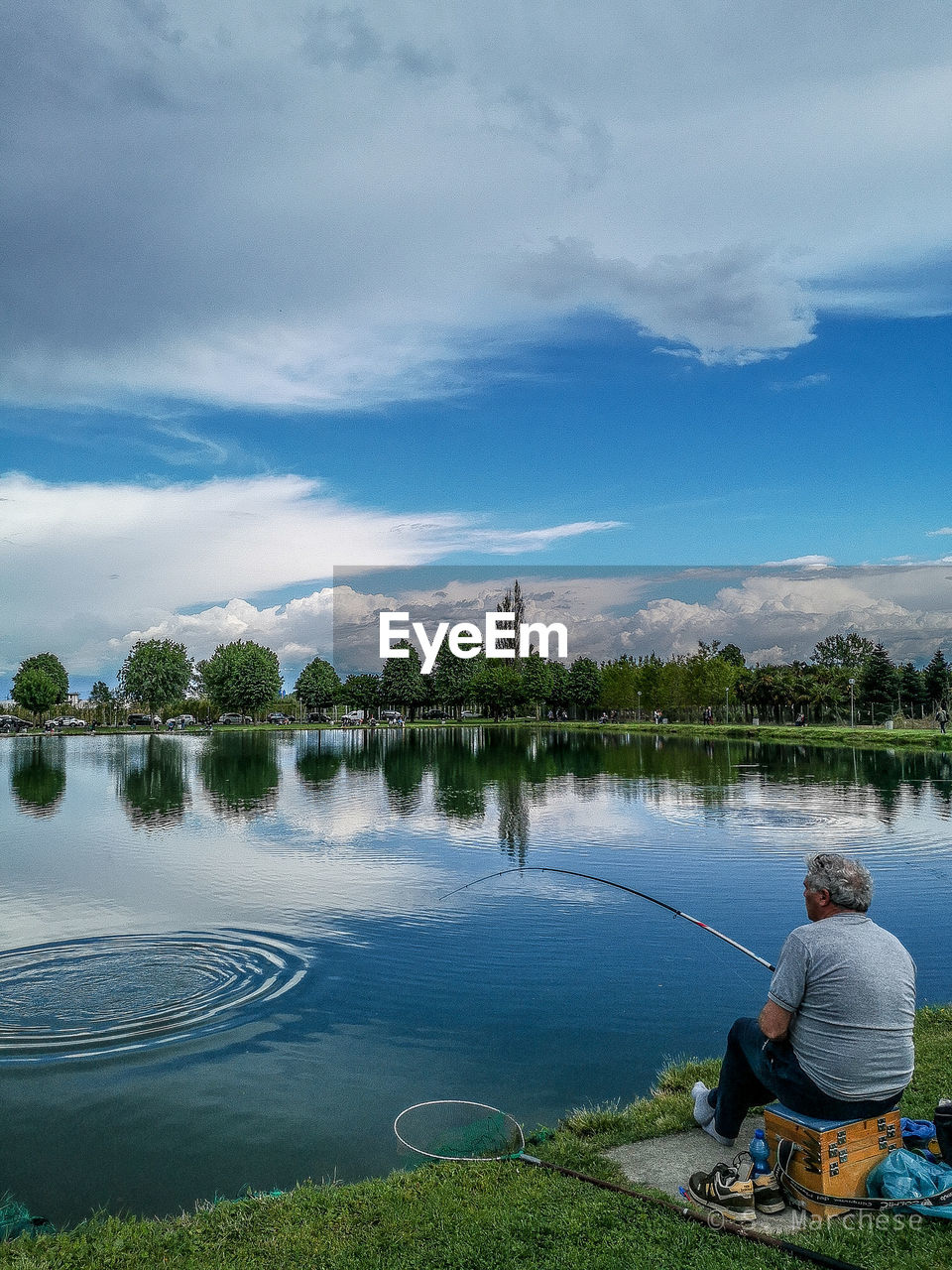 Man fishing in lake against cloudy sky