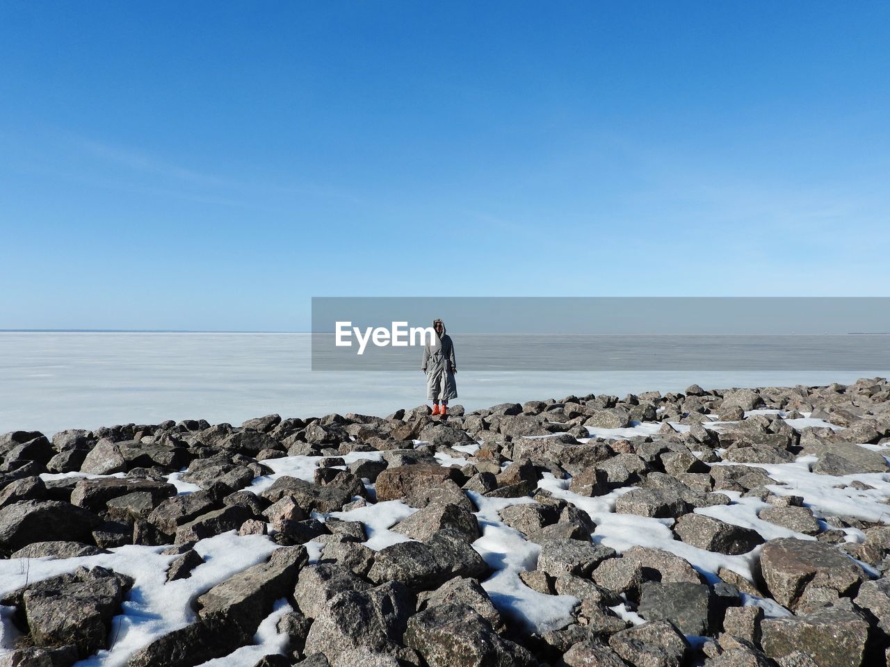 sky, shore, sea, water, coast, ocean, rock, horizon, horizon over water, nature, beach, one person, full length, land, scenics - nature, clear sky, beauty in nature, standing, tranquility, day, copy space, adult, leisure activity, blue, tranquil scene, rear view, holiday, body of water, stone, non-urban scene, vacation, outdoors, lifestyles, trip, women, solitude, environment, sand, bay, idyllic, sunny, travel, sunlight, remote, men, wave, breakwater