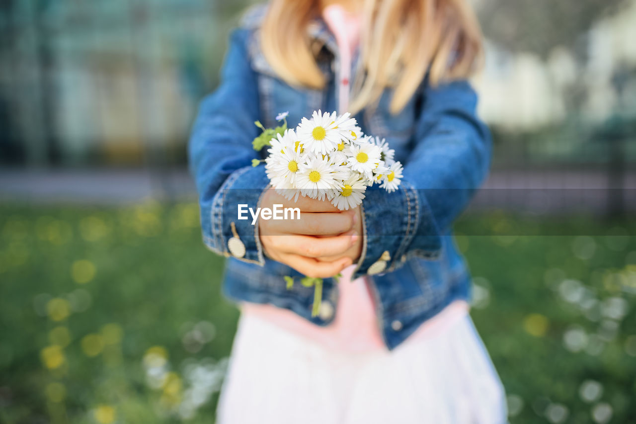 Midsection of girl holding flowers while standing on field