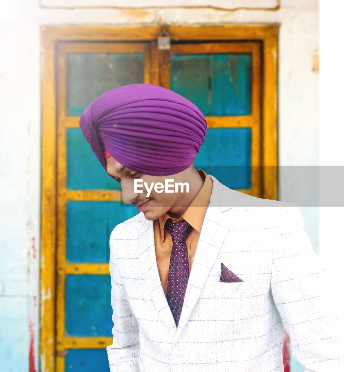 Smiling man in turban and suit standing against door