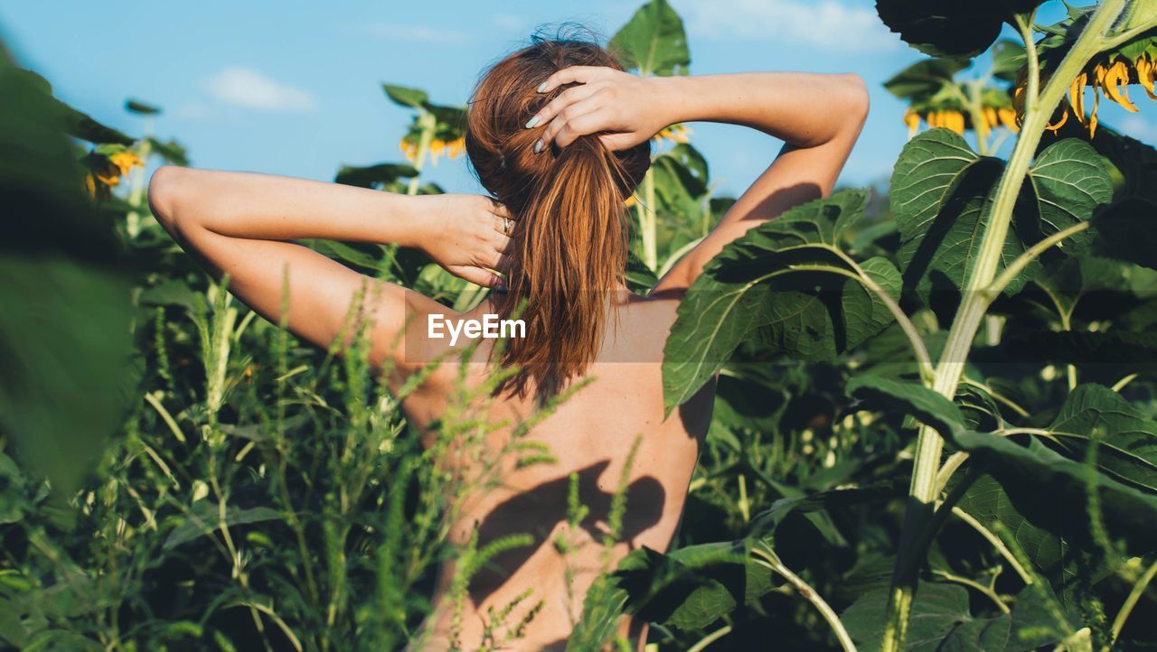 Rear view of topless standing amidst plants