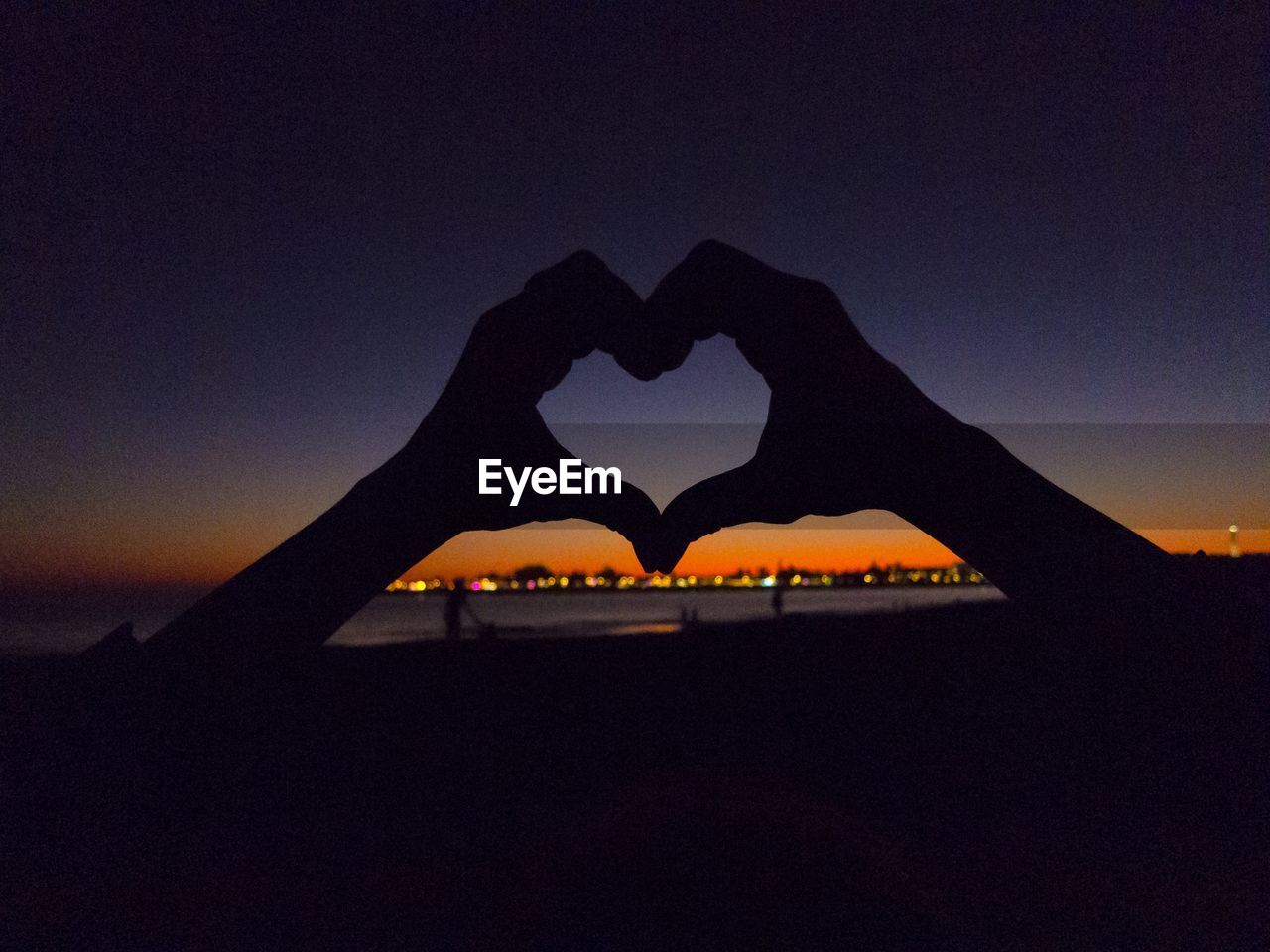 Silhouette hands making heart shape during sunset