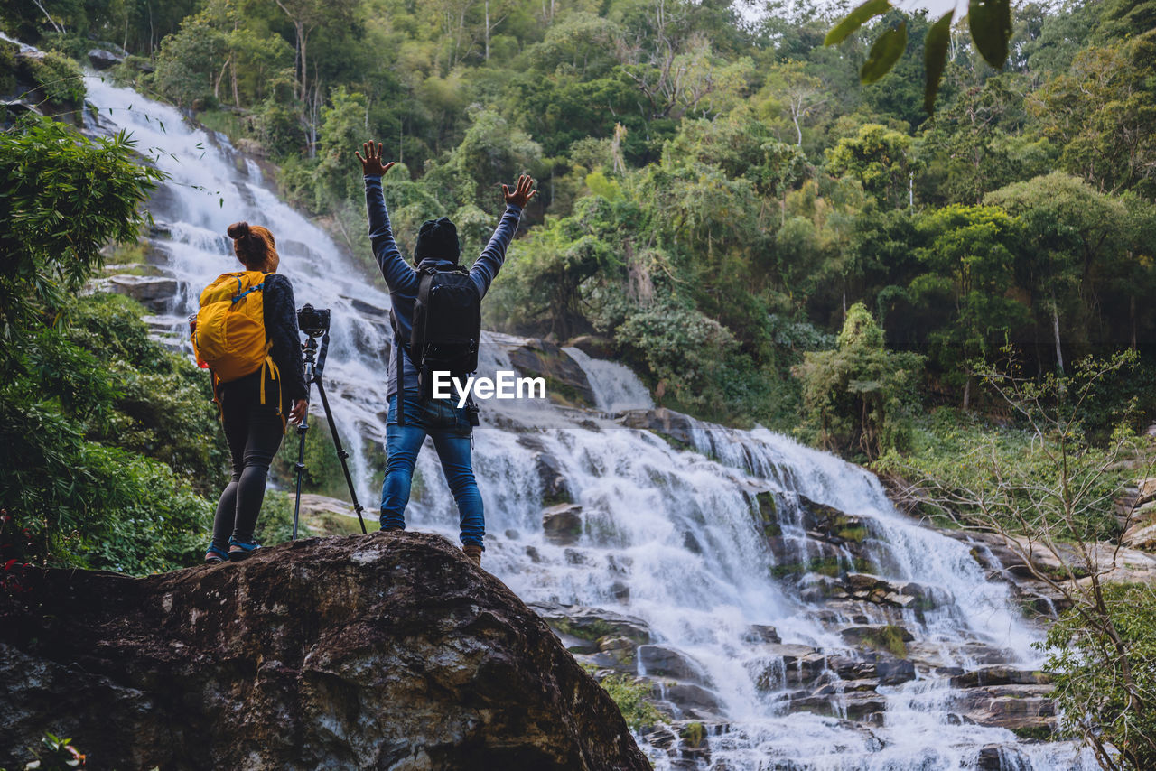 Rear view of friends photographing waterfall in forest