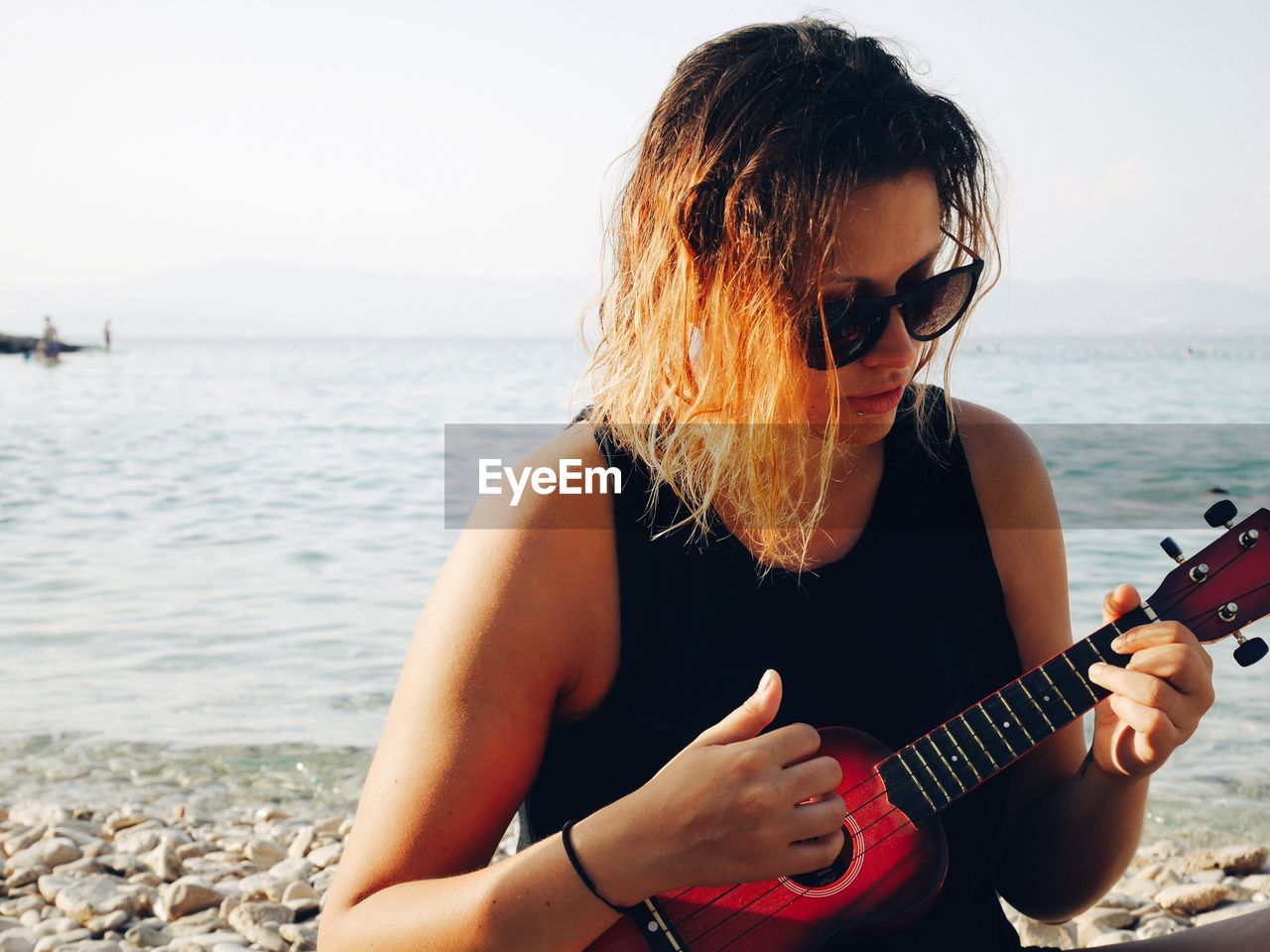 Woman playing guitar at beach against sky
