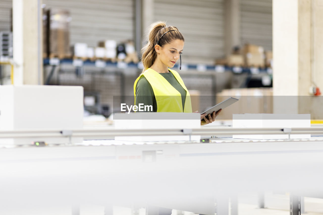 Young worker holding tablet pc analyzing box on conveyor belt in warehouse