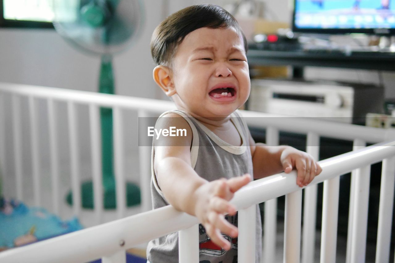 Close-up of baby boy crying in crib at home