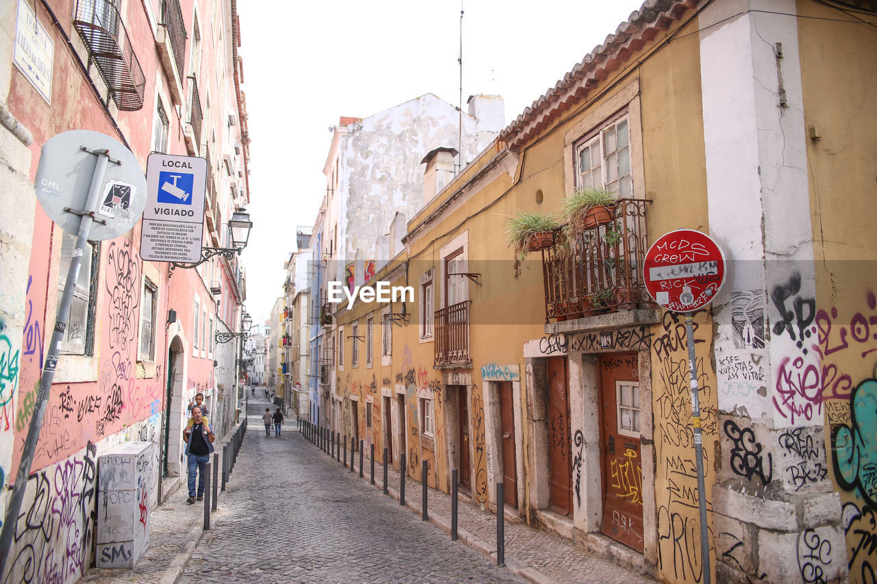 PEOPLE WALKING IN ALLEY AMIDST RESIDENTIAL BUILDINGS