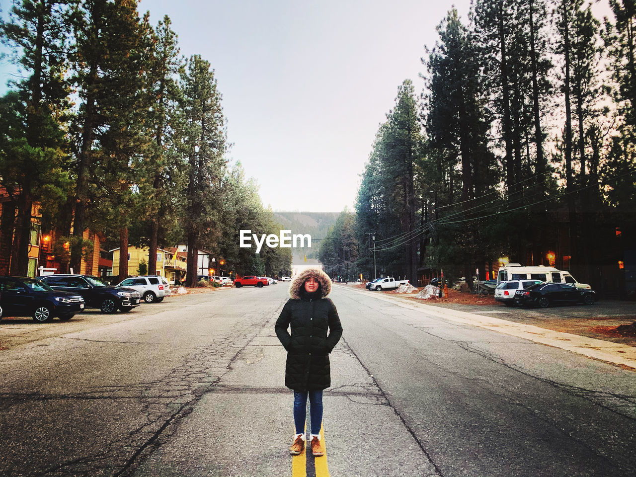 Full length of woman wearing fur hat standing amidst road against trees