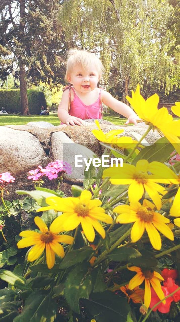 Cute smiling baby girl standing by yellow flowers in park