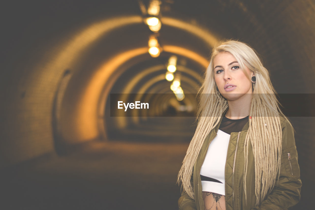 Portrait of young woman standing in illuminated tunnel