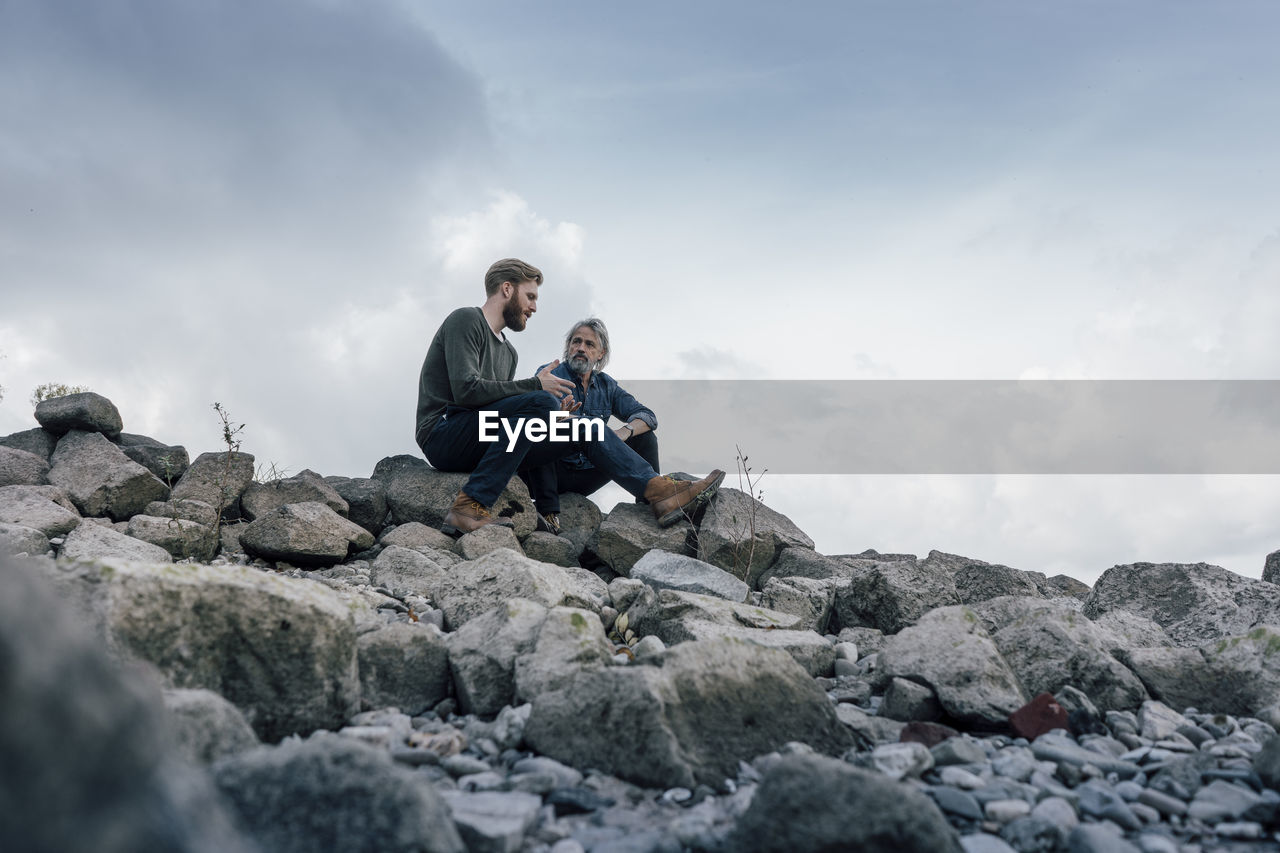 Father and son spending time together outdoors, taking a break, sitting on stones