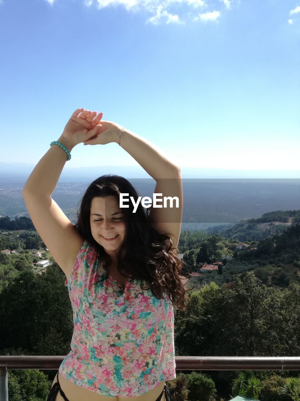 Smiling woman with arms raised standing against sky