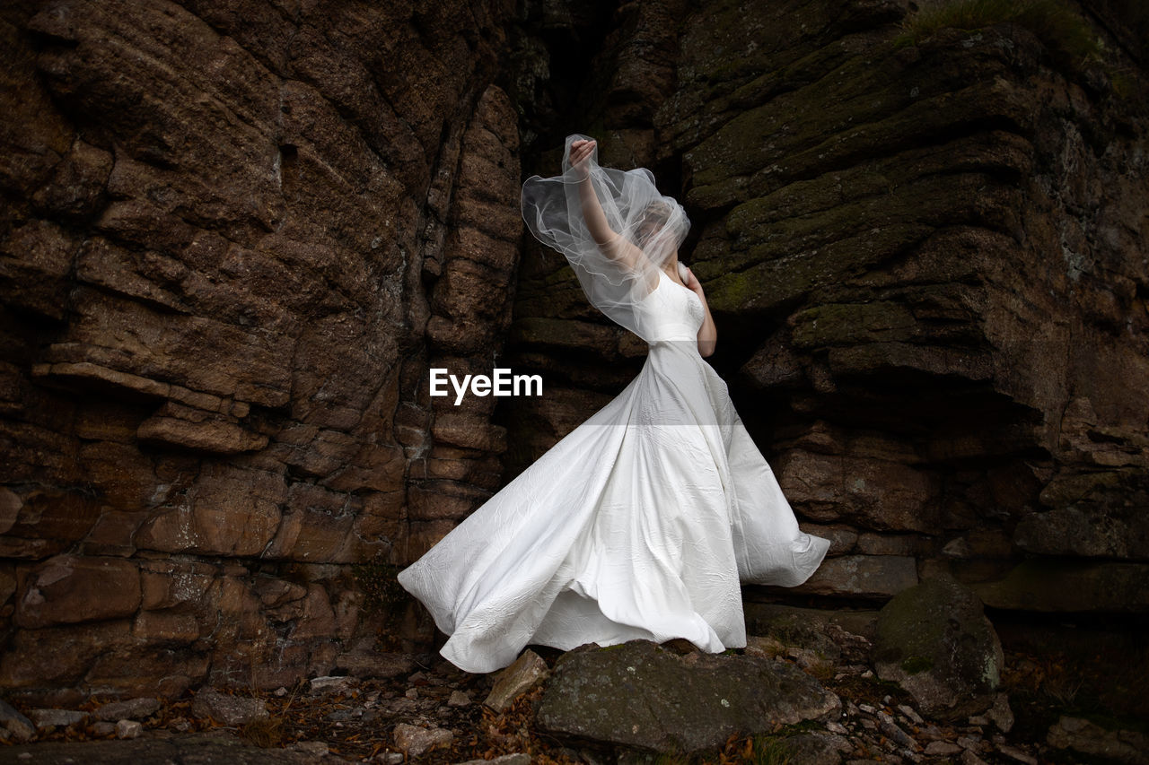 Rear view of woman standing on rock wearing a wedding dress