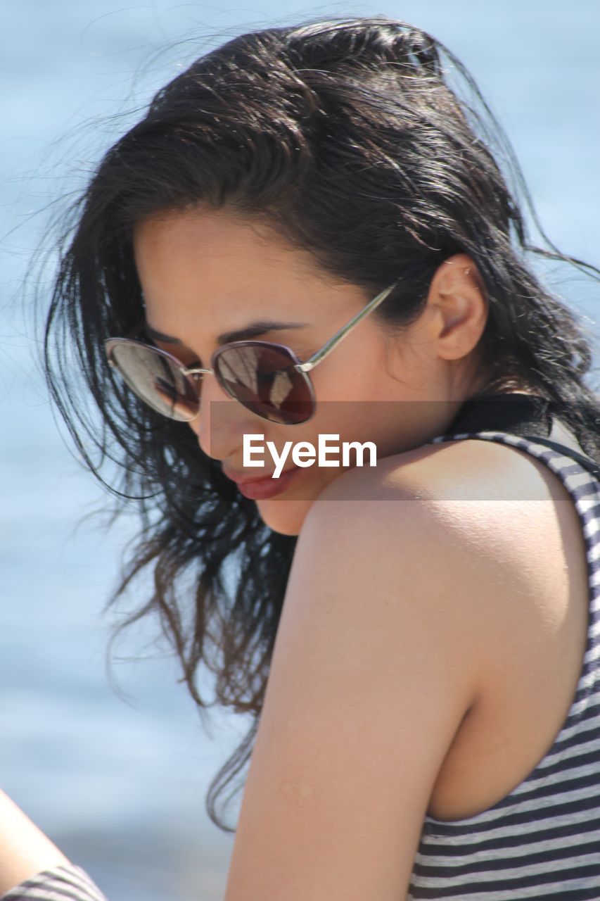 Close-up of woman wearing sunglasses sitting against sea